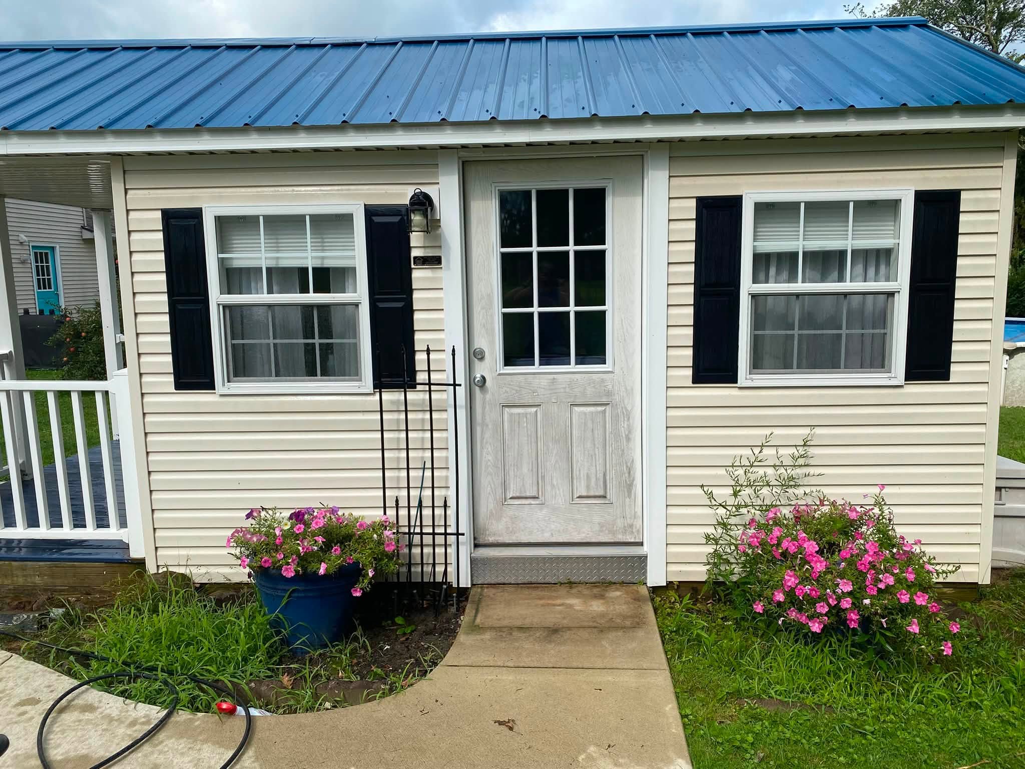 Pool house with cream siding and a blue metal roof looking dull and weathered before washing