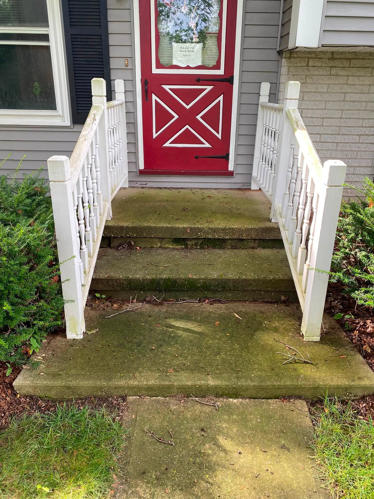 Front steps and porch slab covered in green algae and moss before cleaning