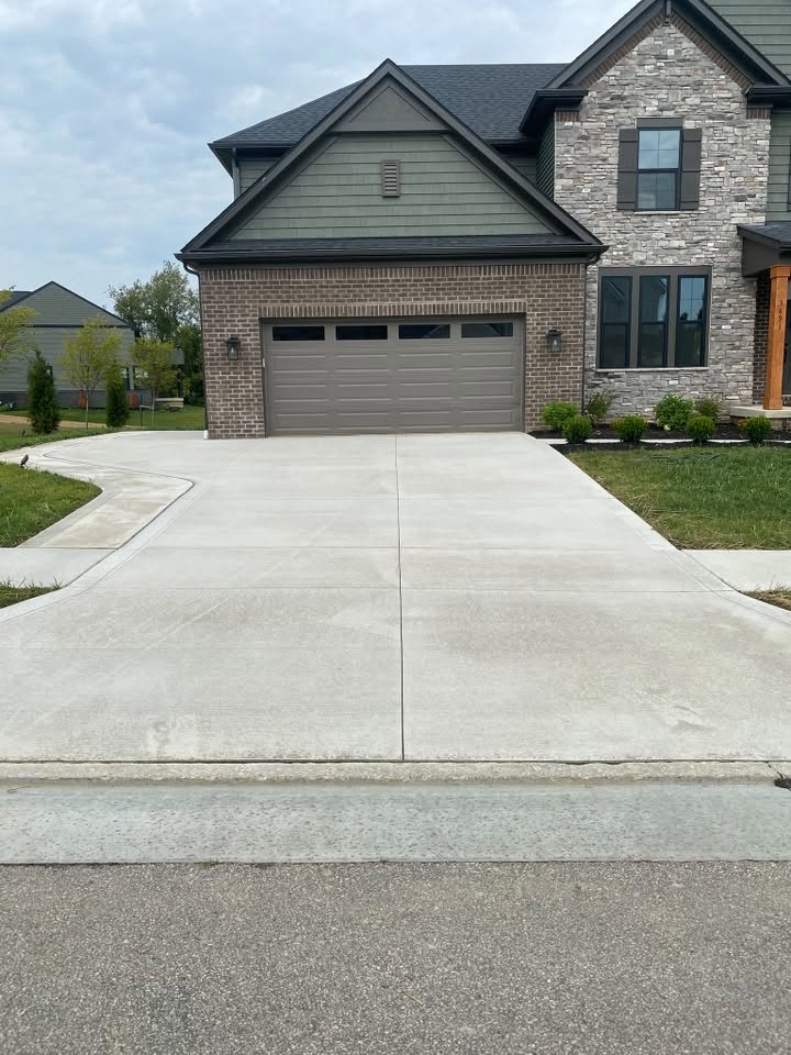 Concrete driveway in front of a brick and stone home, dulled with dirt and tire marks before cleaning