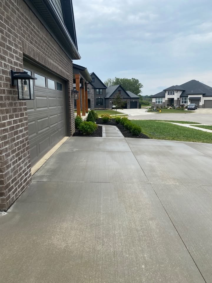 Concrete driveway beside a brick house, still wet from washing, a new-build street visible beyond