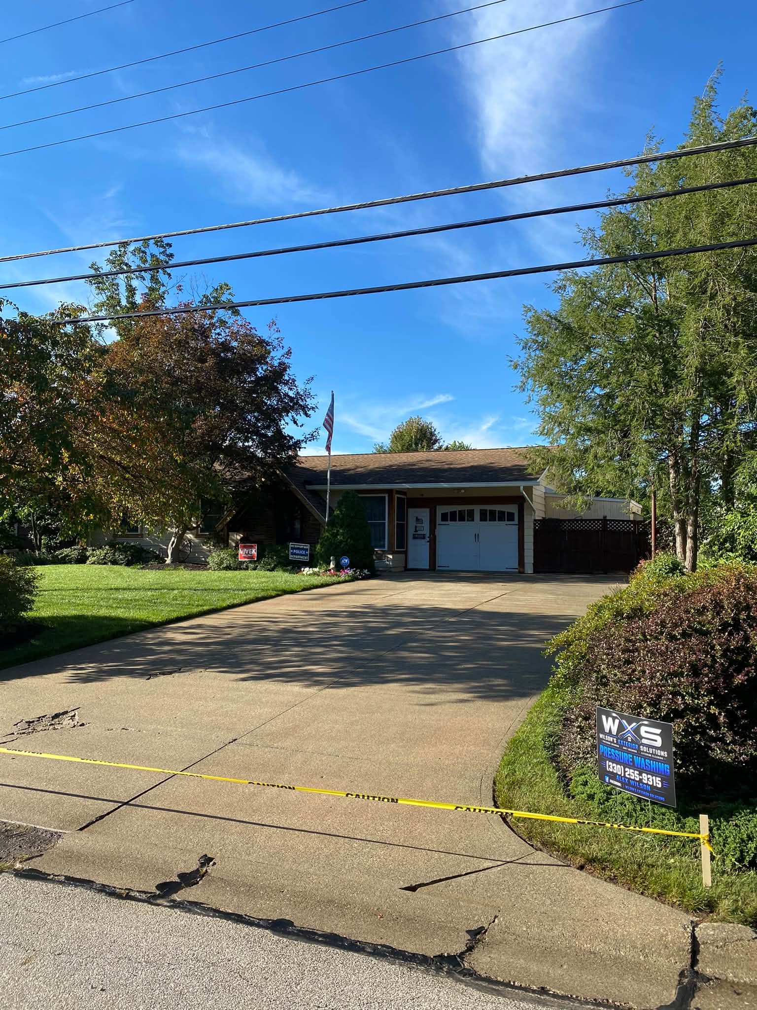 Ranch home with a freshly washed driveway taped off with caution tape while it dries, Wilson's yard sign in the border