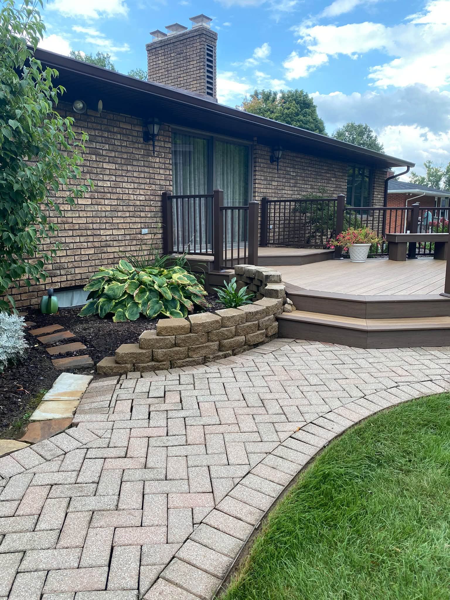 Herringbone paver patio and composite deck steps cleaned around a stone retaining wall and planting bed