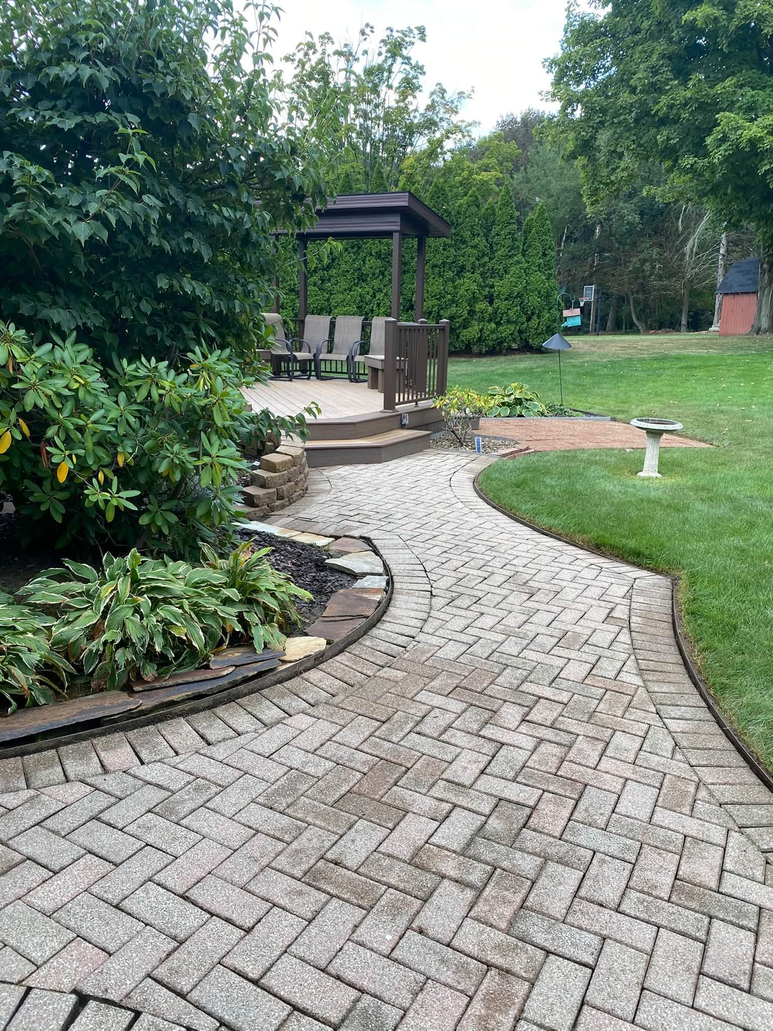 Herringbone brick paver walkway curving across a lawn to a covered gazebo deck with chairs