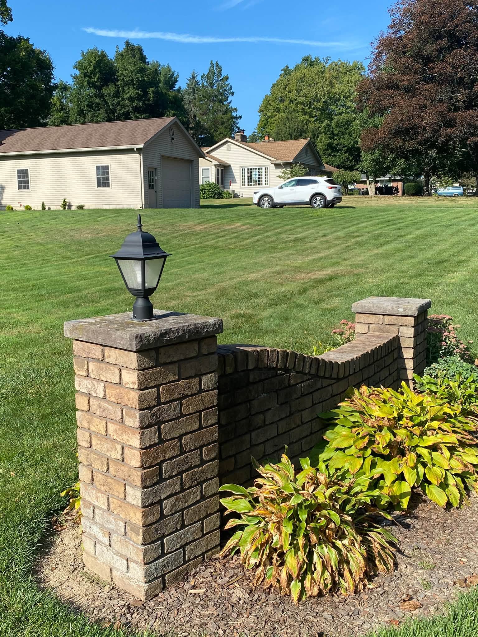 Brick entrance pillar and wall at the end of a wide lawn on a clear day